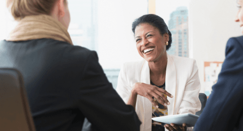 A smiling woman wearing a white blazer in a meeting.